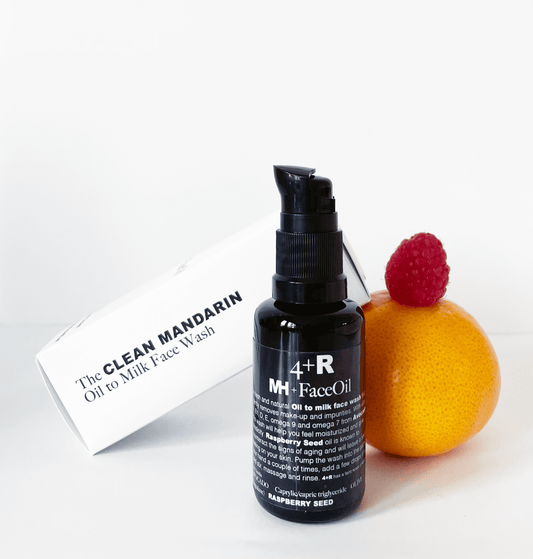Black bottle of face oil with a raspberry and mandarin on a white background