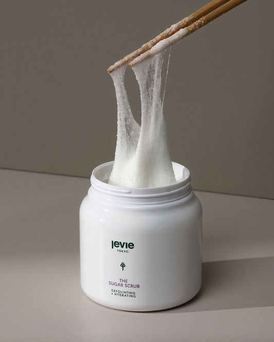 White jar of sugar scrub with a wooden spoon lifting a scoop out, on a neutral background.