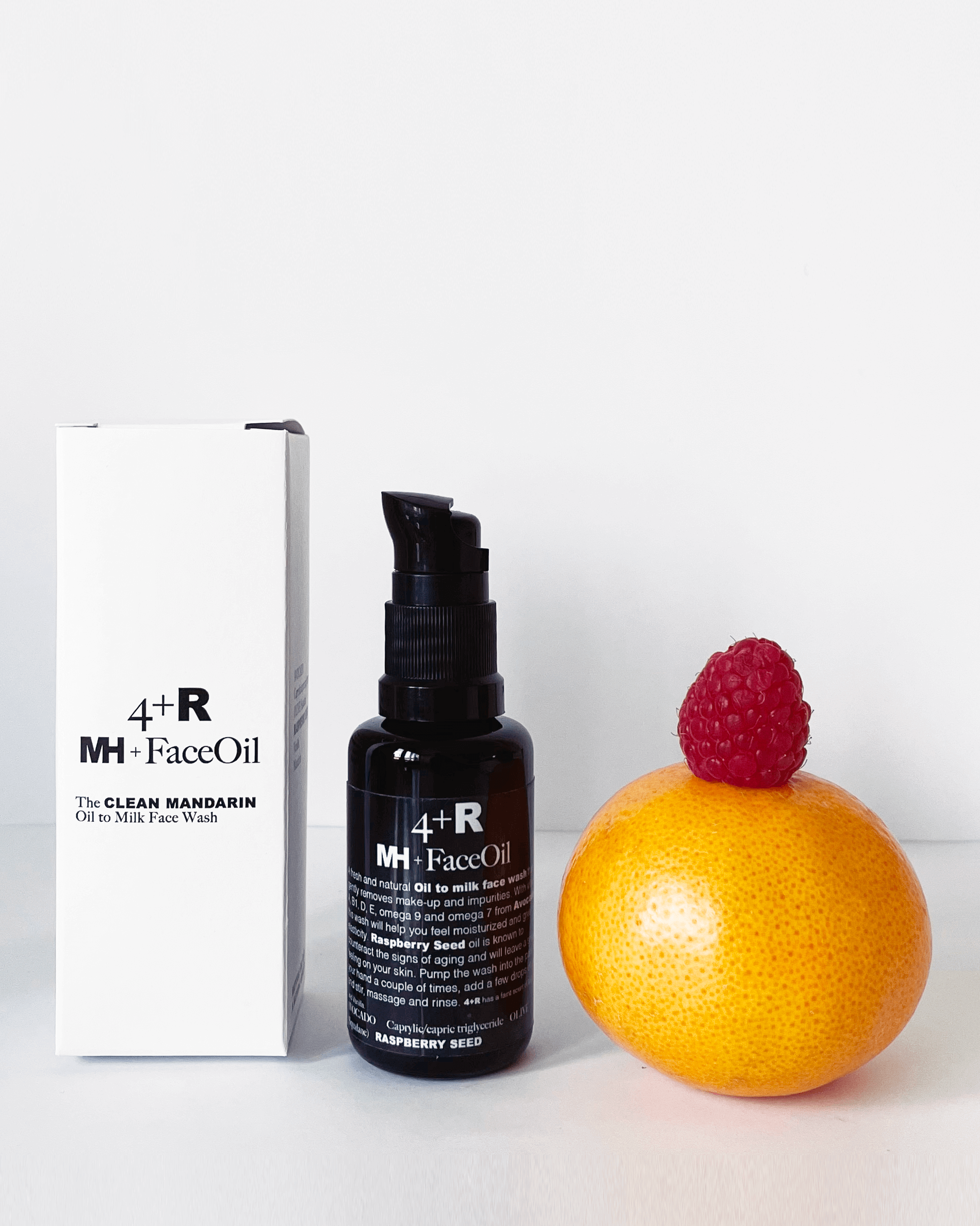 MH Face Oil bottle with packaging and a raspberry on an orange against a white background