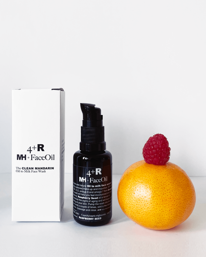 MH Face Oil bottle with packaging and a raspberry on an orange against a white background