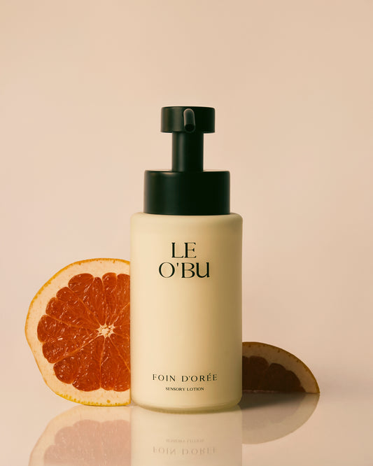 Le O'Bu bottle with a black pump on a beige background with a sliced grapefruit.