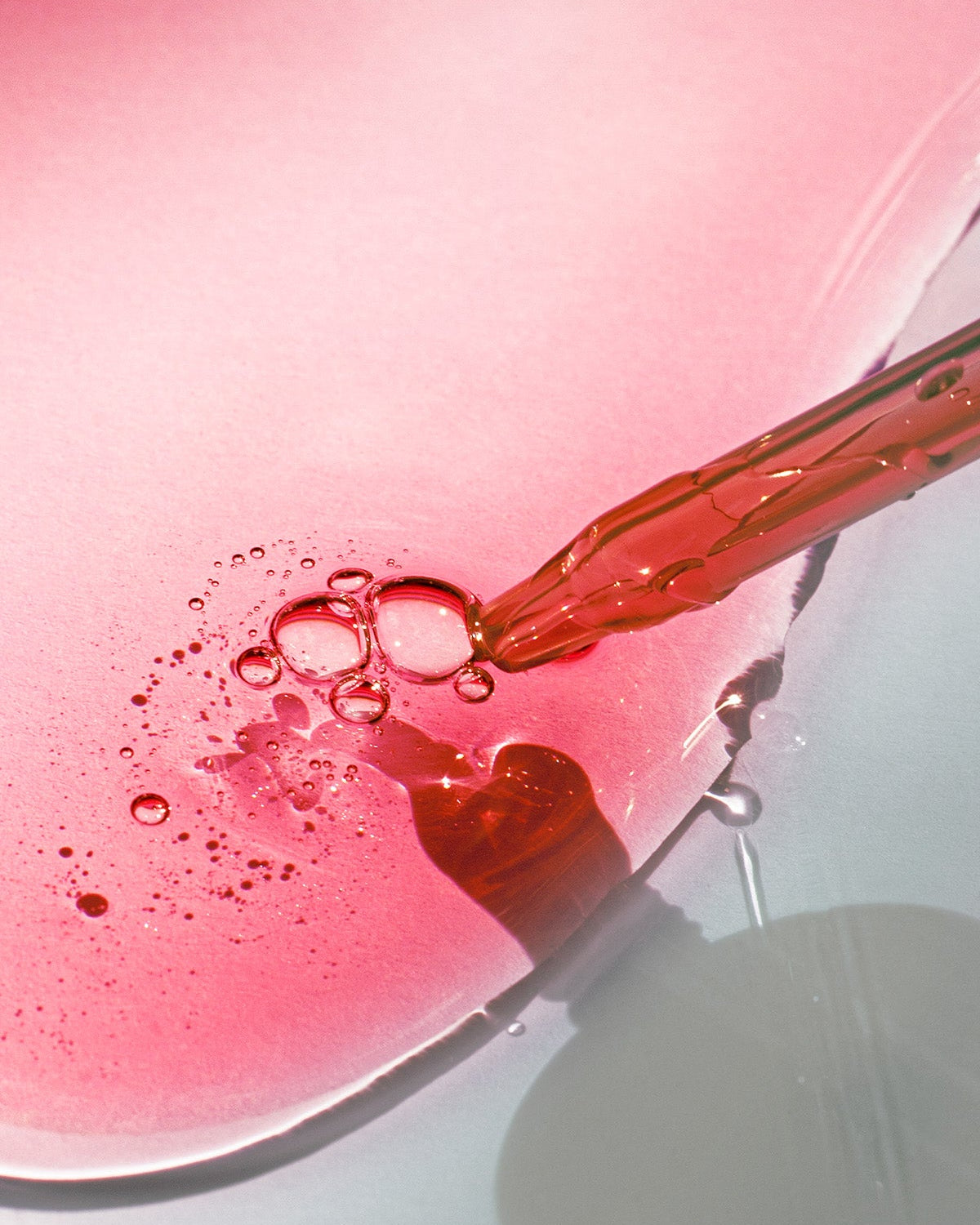 Red liquid being piped onto a pink surface with bubbles