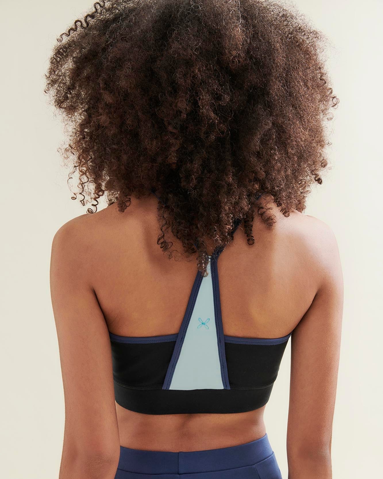 Person wearing a black sports bra with geometric design and blue leggings on a beige background