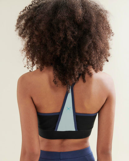Person wearing a black sports bra with geometric design and blue leggings on a beige background