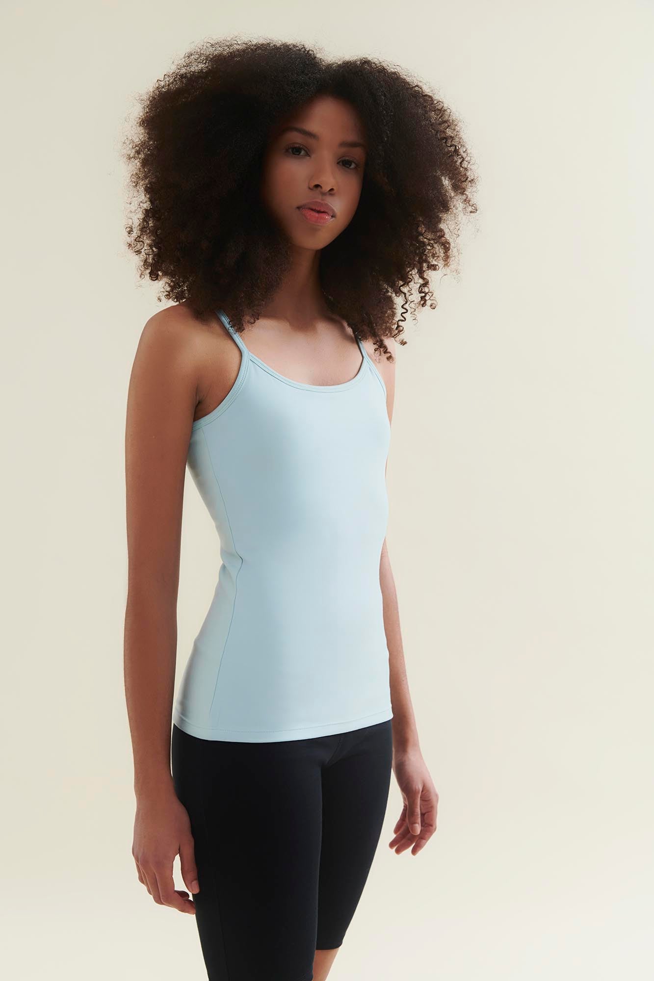 Woman wearing a light blue tank top and black leggings against a beige background