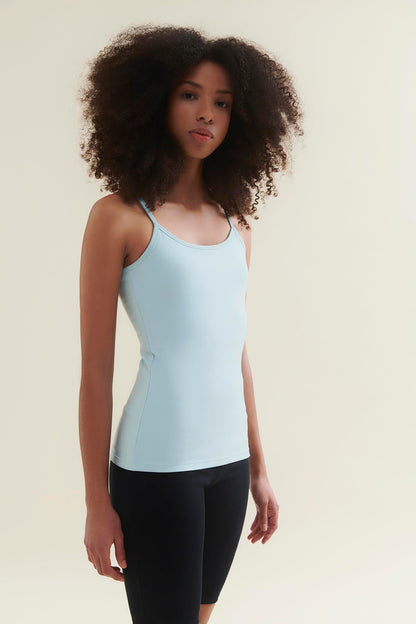 Woman wearing a light blue tank top and black leggings against a beige background