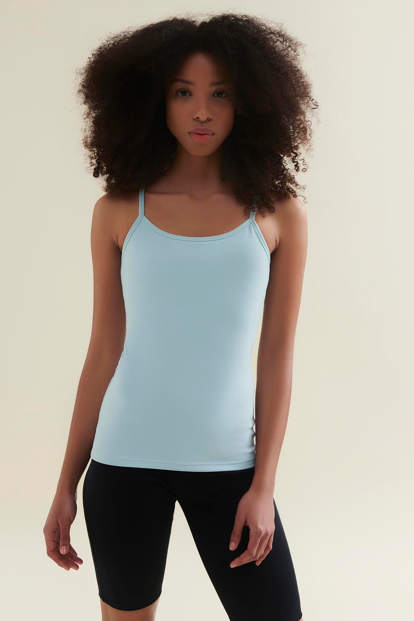 Woman wearing a light blue tank top and black shorts on a beige background